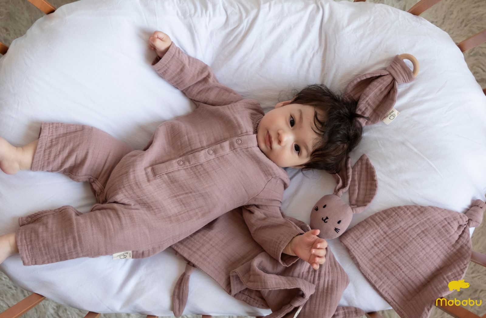 Baby in Overall liegt auf einem Kissen. Was zieht man einem Baby unter dem Schlafsack an?