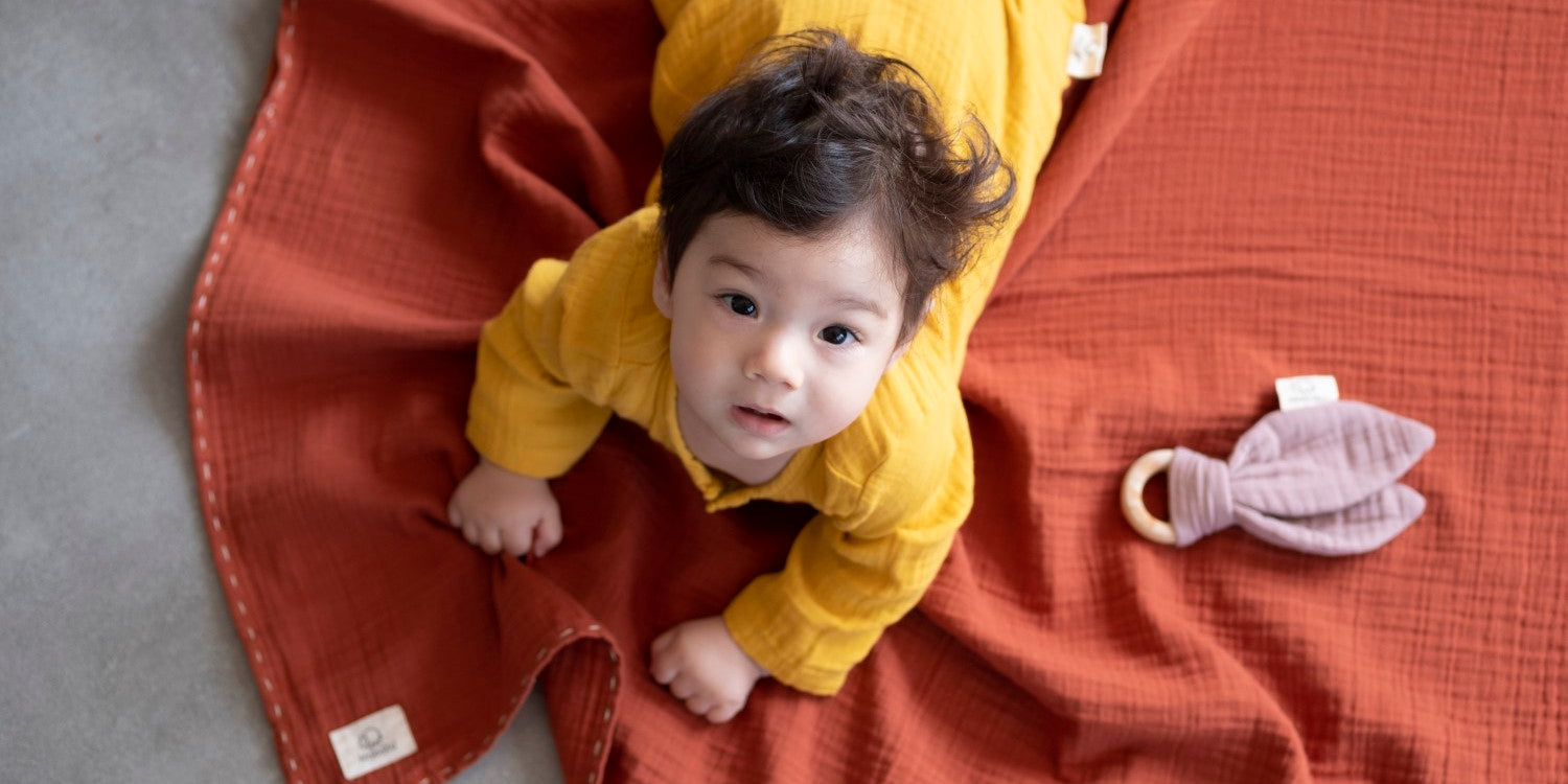 Cute boy with mustard yellow muslin jumper, dusty rose wood teether and rust muslin playing cloth.